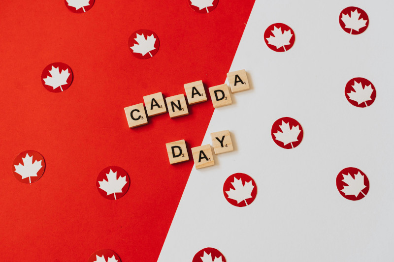 Canada Day text surrounded by red maple leaves and flag-themed background